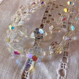 May include: A strand of iridescent crystal beads, with a faceted, diamond-like shape. The beads are strung on a clear thread and are arranged in a loose, flowing pattern.