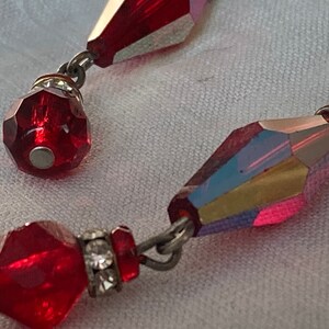 Puede incluir: Un par de pendientes colgantes con cuentas de cristal facetadas rojas y detalles en metal plateado.