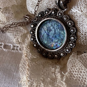 May include: A silver pendant necklace with a round, iridescent glass cabochon set in a silver frame. The frame is decorated with a beaded border.