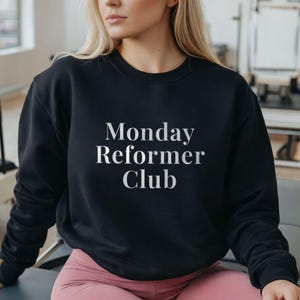 May include: Black crew neck sweatshirt with the text "Monday Reformer Club" in white. The sweatshirt is made of a soft material and is suitable for casual wear. The image shows the sweatshirt on a person.