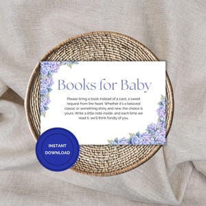 Könnte beinhalten: Eine weiße Karte mit dem Text "Books for Baby" und der Bitte, ein Buch statt einer Karte mitzubringen. Die Karte ist mit Aquarellblumen in Blau und Lila verziert und liegt auf einem geflochtenen Korb.