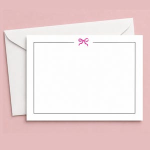 May include: A white rectangular stationery card featuring a thin black border and a small pink bow icon centered at the top edge. The card is positioned in front of a matching white envelope, providing a clean and simple design for written notes.