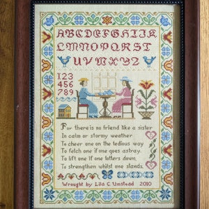 Könnte beinhalten: Ein gerahmter Kreuzstich-Sampler mit einem bunten Alphabet, Zahlen und einem Gedicht über die Bedeutung von Schwesternschaft. Das Gedicht lautet: "Denn es gibt keinen Freund wie eine Schwester In ruhigem oder stürmischem Wetter Um einen auf dem mühsamen Weg zu ermutigen Um einen zu holen, wenn einer in die Irre geht. Um einen zu heben, wenn einer taumelt, Um zu stärken, während einer steht." Der Sampler ist signiert mit "Wrought by Lila C. Umstead 2010".