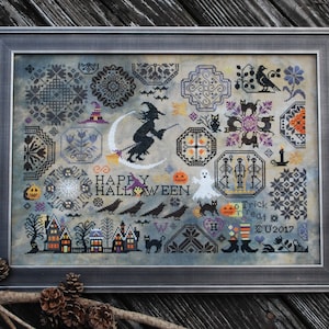 May include: Framed cross-stitch artwork with a Halloween theme. The design includes a witch on a broom, a crescent moon, pumpkins, ghosts, and the words "Happy Halloween". The artwork is in a grey frame.