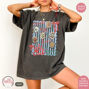 May include: Dark grey t-shirt with a graphic featuring Mahjong tiles, the text "Snacks, dots, bams, Mahj Club" and the phrase "if you know, you know!" in red and blue. The shirt has a vintage, worn look.