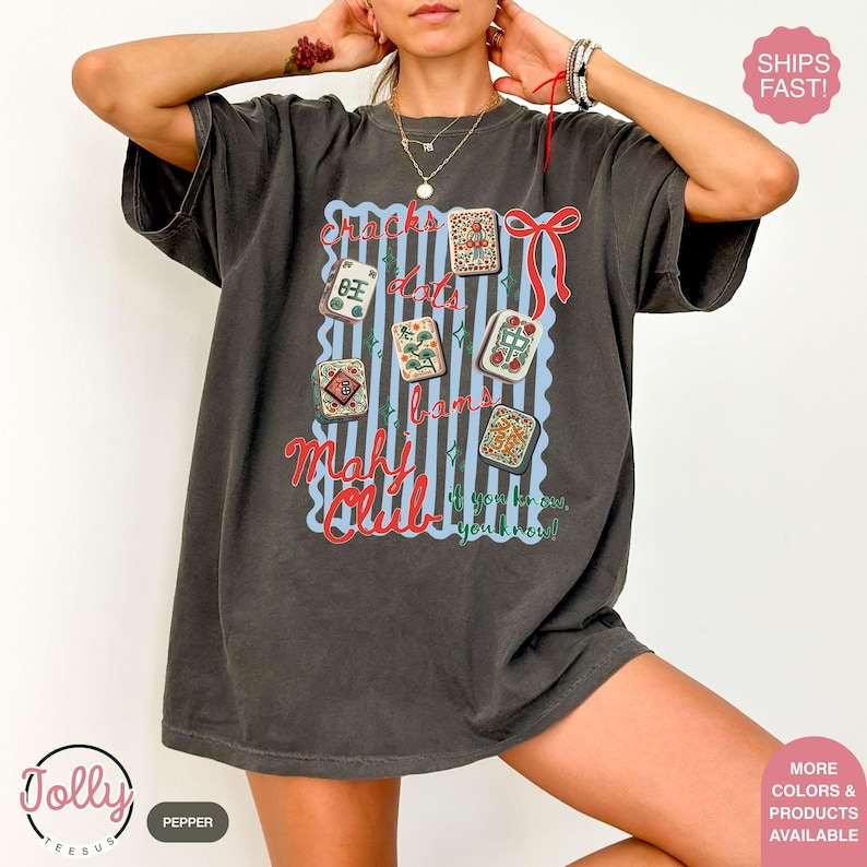 May include: Dark grey t-shirt with a graphic featuring Mahjong tiles, the text "Snacks, dots, bams, Mahj Club" and the phrase "if you know, you know!" in red and blue. The shirt has a vintage, worn look.