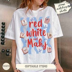 May include: A white short-sleeve t-shirt featuring the red text "red white and Mahj" surrounded by blue wavy lines, small firecracker illustrations, and six mahjong tiles with patriotic designs. A tag in the corner reads "group matching shirts".