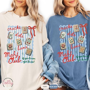 May include: Two long-sleeved t-shirts, one ivory and one blue jean, featuring a graphic design. The design includes the words "cracks, dots, bams, Mahj Club" with decorative elements and the phrase "if you know, you know!"