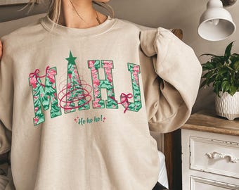 May include: A beige crewneck sweatshirt featuring the letters MAHJ in a varsity font. The letters are filled with a green and pink Christmas tree pattern. A pink string graphic wraps around the letters, and the text Ho ho ho! is printed below.