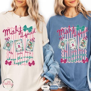 May include: Two long-sleeved shirts, one ivory and one blue jean, feature a graphic with the text "Mahj Squad" and "where the magic happens!". The design includes three Mahjong tiles and bows.