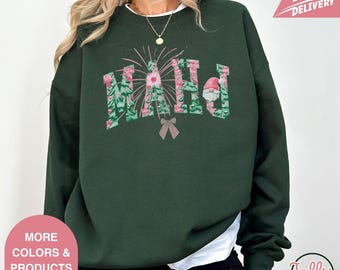 May include: Dark green sweatshirt with the word "MAHJ" in a floral design with a Santa hat on the letter "J". A pink bow is below the letters. The sweatshirt has a crew neck and long sleeves. The image also includes text that says "More Colors & Products Available" and "Fast Delivery".