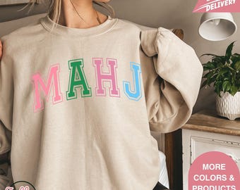 May include: Beige sweatshirt with the word "MAHJ" in pink, green, and blue block letters. The sweatshirt has a crew neck and long sleeves. The Jolly Tees logo is visible in the bottom left corner.