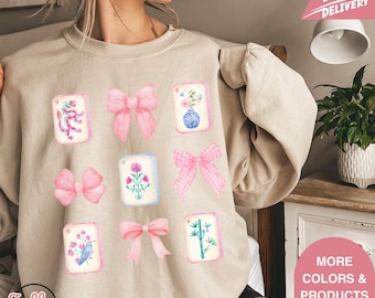 May include: Beige sweatshirt featuring a collection of watercolor illustrations. The design includes pink bows and decorative tiles with floral and animal motifs. The text "Jolly Teesub" is visible at the bottom left.