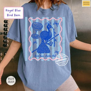 May include: A blue t-shirt with a peacock graphic, a cocktail glass, and the text "bird bam cheers club." The shirt also features the text "Royal Blue Bird Bam" and "BLUE JEAN."