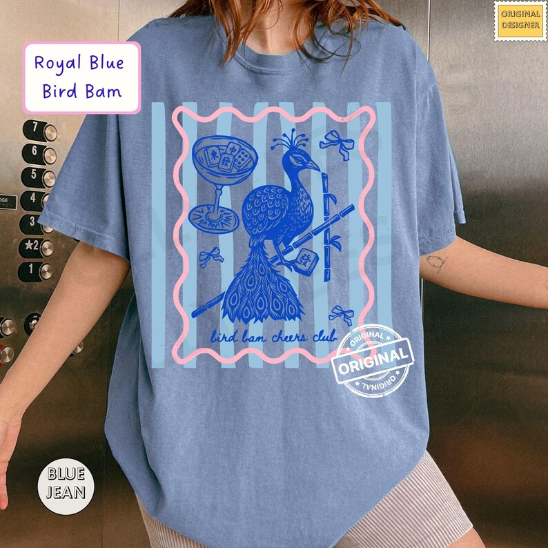 May include: A blue t-shirt with a peacock graphic, a cocktail glass, and the text "bird bam cheers club." The shirt also features the text "Royal Blue Bird Bam" and "BLUE JEAN."