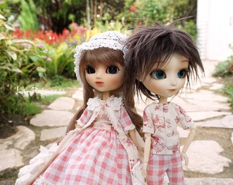 Peut inclure: Deux poupées, l'une portant une robe en vichy rose et blanche avec une bordure en dentelle blanche et un chapeau en dentelle blanche, et l'autre portant une chemise et un short en vichy blanc et rouge avec des chaussettes rayées noires et blanches et des chaussures noires.