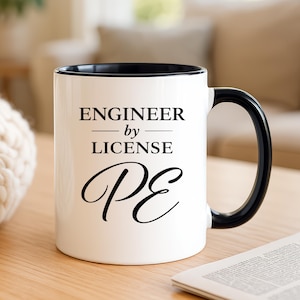 May include: White ceramic mug with a black interior and handle. The mug features the text "ENGINEER by LICENSE PE" in black, with a serif font. The mug is on a wooden surface.