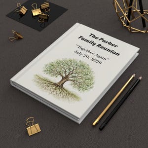 May include: A white journal with the text "The Parker Family Reunion" and "Together Again" July 20, 2026. The cover features a watercolor illustration of a tree with roots. Gold and black pencils and gold binder clips are also visible.