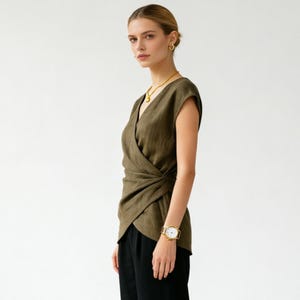 May include: Olive green wrap top with a V-neck design. The top is paired with black pants. A gold necklace, earrings, and a wristwatch with a gold band and white face complete the look. The outfit is simple and elegant.