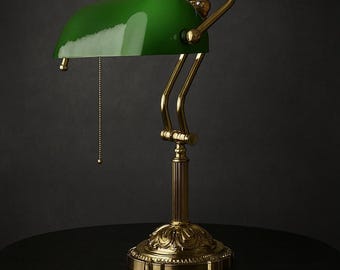 May include: A classic banker's lamp with a glossy green shade and a brass-colored base. The lamp features a pull chain and a decorative base. The lamp is on a black surface.
