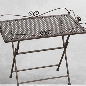 Puede incluir: Una mesa plegable de metal marrón con una parte superior rectangular perforada. La mesa tiene adornos decorativos en la parte superior y los lados. Las patas están en ángulo y se pliegan para guardarla.