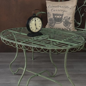 May include: A vintage-style, light green metal patio set with a round table and a bench. A black alarm clock sits on the table. A pillow with "Cinderella's Carriage" text rests on the bench.