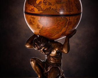 May include: A decorative globe featuring a detailed map design in shades of brown and orange. The globe is supported by a bronze-colored statue of Atlas, kneeling and holding the globe overhead. The base is a dark, round wooden platform.