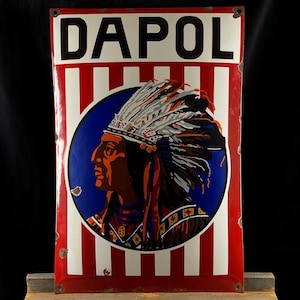 May include: A vintage Dapol sign featuring a Native American profile within a blue circle, set against a red and white striped background. The word "DAPOL" is in white at the top. The sign shows signs of age and wear.