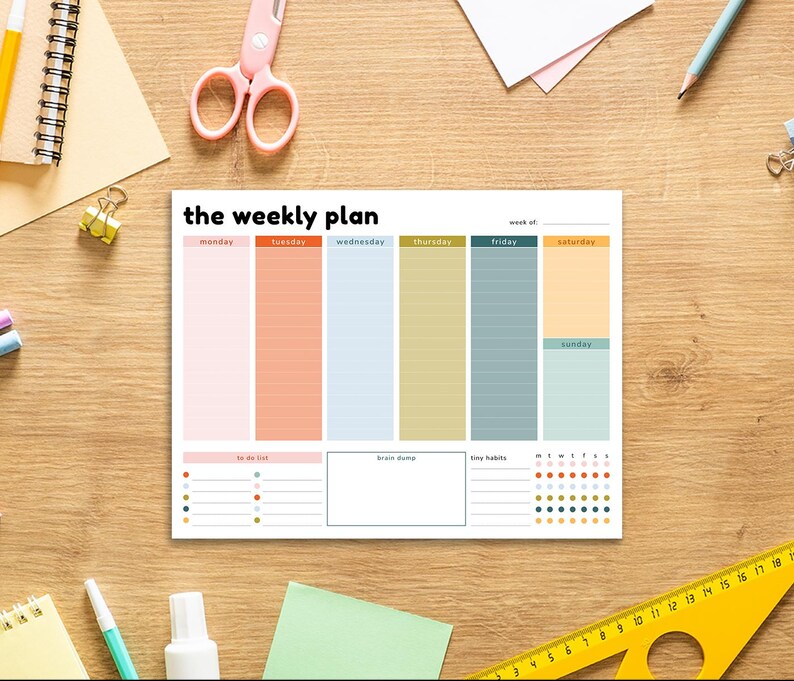 Puede incluir: Un planificador semanal con el texto "the weekly plan". Presenta columnas para cada d&iacute;a de la semana, con secciones para listas de tareas, lluvia de ideas y peque&ntilde;os h&aacute;bitos. Sobre una superficie de madera.