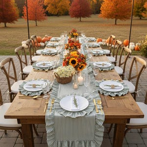 Peut inclure: Une longue table en bois dress&eacute;e pour un repas en plein air &agrave; l'automne. La table est orn&eacute;e d'assiettes blanches, de couverts dor&eacute;s et de sets de table &agrave; rayures vertes et blanches. Des centres de table avec des tournesols et des fleurs d'automne.