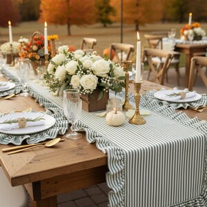 Peut inclure: Une table en bois dress&eacute;e pour une r&eacute;ception, avec un chemin de table &agrave; rayures vertes et blanches. Des assiettes blanches, des couverts dor&eacute;s et des bougies entourent une composition florale de roses blanches. Une petite citrouille blanche ajoute une touche saisonni&egrave;re.