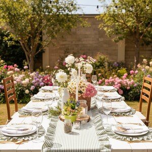 Peut inclure: Une table de salle &agrave; manger ext&eacute;rieure joliment dress&eacute;e avec des assiettes blanches, des verres et des couverts. La table est d&eacute;cor&eacute;e d'un chemin de table &agrave; rayures vertes et blanches, de compositions florales et de bougies. Le cadre est un jardin avec des arbres et des fleurs.