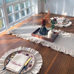 Soft ruffled table runner in white linen, styled for spring table decor and cozy gatherings. This French table runner complements french tablecloth and boho table runner themes. Ideal as a christmas runner, halloween tablecloth, or everyday white runner. A charming french tablecloth look, perfect for French table runner lovers and unique ruffled runner designs.