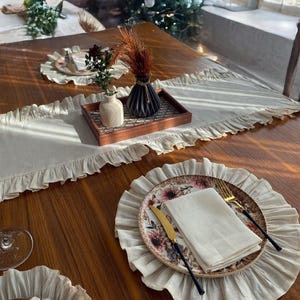 Soft ruffled table runner in white linen, styled for spring table decor and cozy gatherings. This French table runner complements french tablecloth and boho table runner themes. Ideal as a christmas runner, halloween tablecloth, or everyday white runner. A charming french tablecloth look, perfect for French table runner lovers and unique ruffled runner designs.