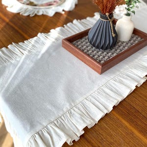 Soft ruffled table runner in white linen, styled for spring table decor and cozy gatherings. This French table runner complements french tablecloth and boho table runner themes. Ideal as a christmas runner, halloween tablecloth, or everyday white runner. A charming french tablecloth look, perfect for French table runner lovers and unique ruffled runner designs.