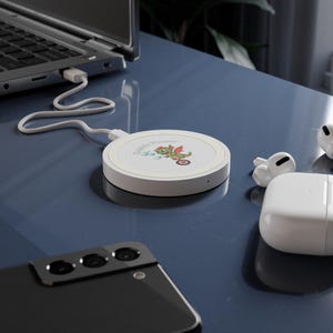 Op de afbeelding: Een witte draadloze oplader met een groene draakillustratie en de tekst "Bubble Power". Een zwarte smartphone, witte draadloze oordopjes en een laptop zijn ook op de afbeelding te zien.