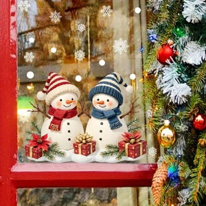 May include: Two snowman figurines wearing hats and scarves, with small gift boxes and poinsettias. The snowmen are on a red shelf, with a Christmas tree and snowflakes in the background. Festive holiday decor.