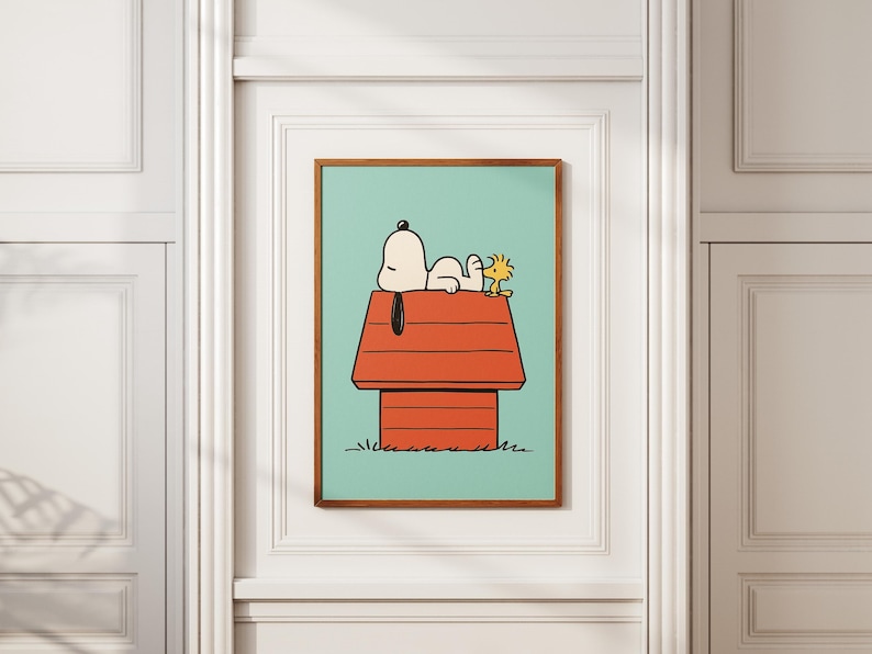 May include: A framed art print depicting Snoopy and Woodstock. Snoopy is resting on his red doghouse, with Woodstock beside him. The background is a light teal, and the frame is brown.