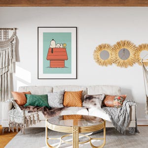 May include: A living room with a beige sofa, cushions, and a framed Snoopy print. A round coffee table, macrame wall hanging, and a hanging chair are visible. The room has a neutral colour palette with wooden accents and a rug. The room is well lit.