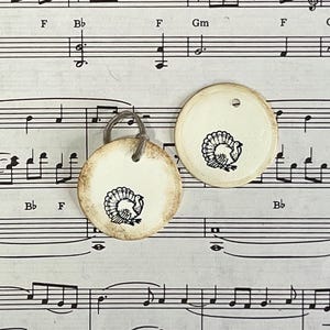 Two round cream gift tags featuring hand-stamped black turkey designs on vintage sheet music. Each tag has softly distressed edges, a subtle raised border and a cord tie.