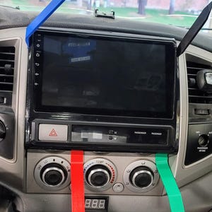 May include: A black car dashboard with a touchscreen display, three round knobs with red, green, and blue trim, and a digital display showing 8.8.8.