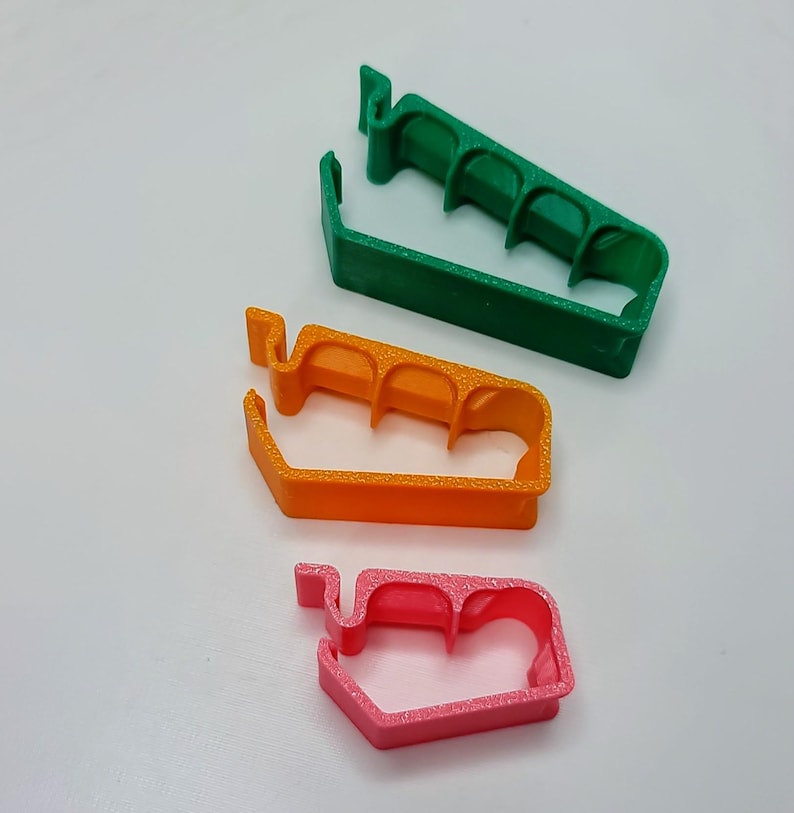 May include: Three plastic cable clips in different sizes. The largest clip is green, the middle clip is orange, and the smallest clip is pink.