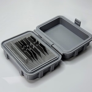 May include: An open, gray plastic storage box with a hinged lid. Inside, a tray with a slotted design holds several metal blades. The box is designed to protect and organize the blades.