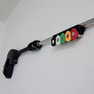 May include: A black pressure washer wand with a silver extension pole and a holder with five different colored spray nozzles. The holder is attached to the wall.