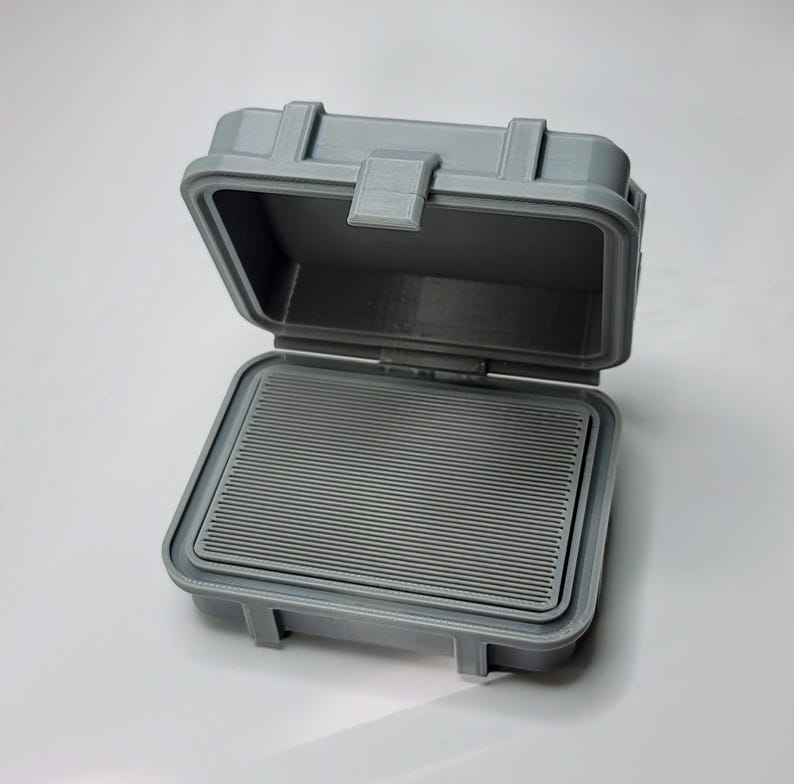 May include: Open gray plastic case with a rectangular interior and a ridged insert. The case has a hinged lid with a latch closure. The case is designed to protect the contents inside.