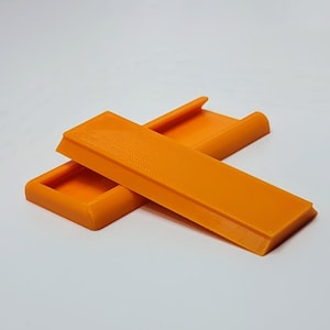May include: Two bright orange rectangular objects are displayed against a white background. One object is positioned horizontally, while the other is angled diagonally across it. The objects have a textured surface and a raised edge.