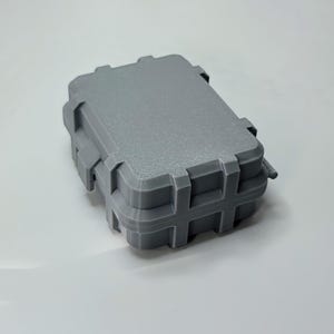 May include: A gray, rectangular, small storage case with a textured surface. The case has a hinged lid and a secure latching mechanism. The case is designed to protect its contents and is suitable for various applications.