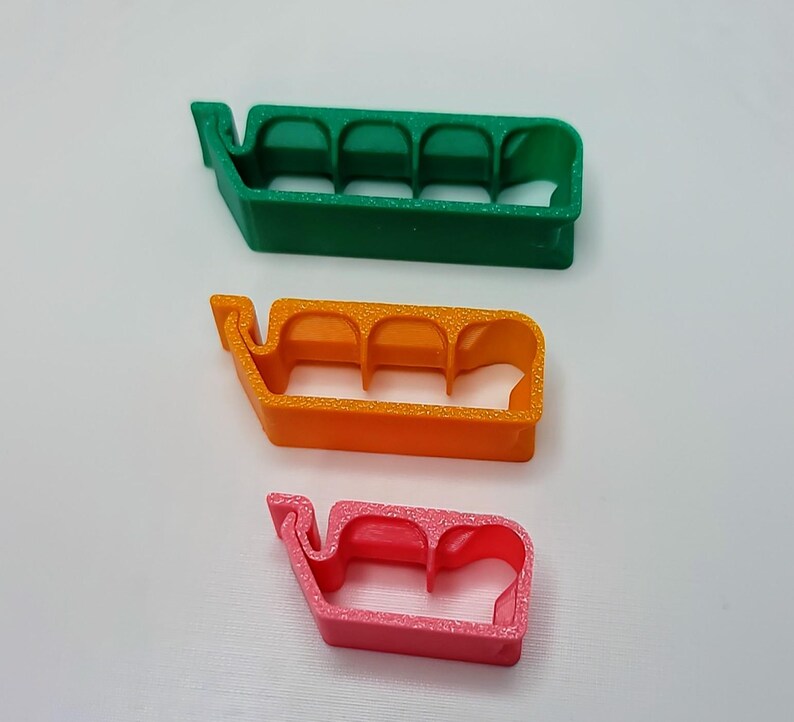 May include: Three plastic cable organizers in different colors: green, orange, and pink. Each organizer has four slots for holding cables.