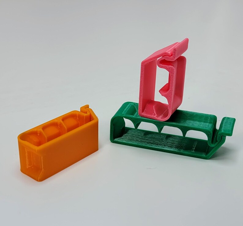 May include: Three 3D printed plastic cable clips in orange, green, and pink. The clips are designed to hold cables in place.