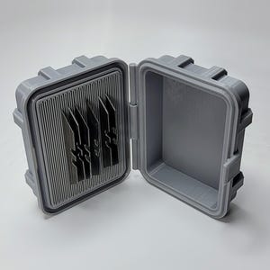 May include: Open gray plastic case with a ribbed interior and several dark gray, blade-like objects. The case is open, revealing the interior and the objects within. The case has a rectangular shape with a hinged lid.